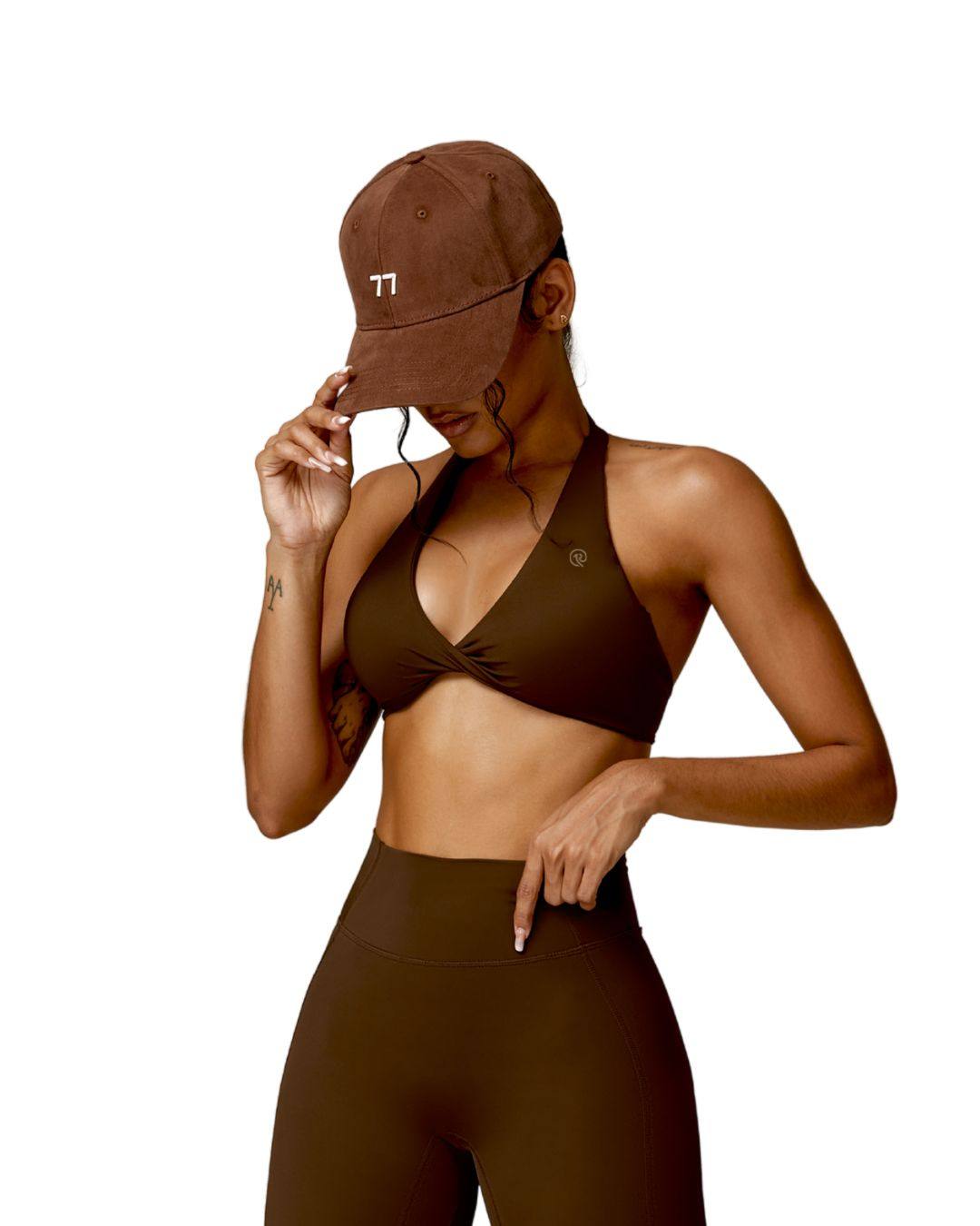 Woman wearing brown ORU Mika halter sports bra with halter neck support and matching leggings with a brown cap