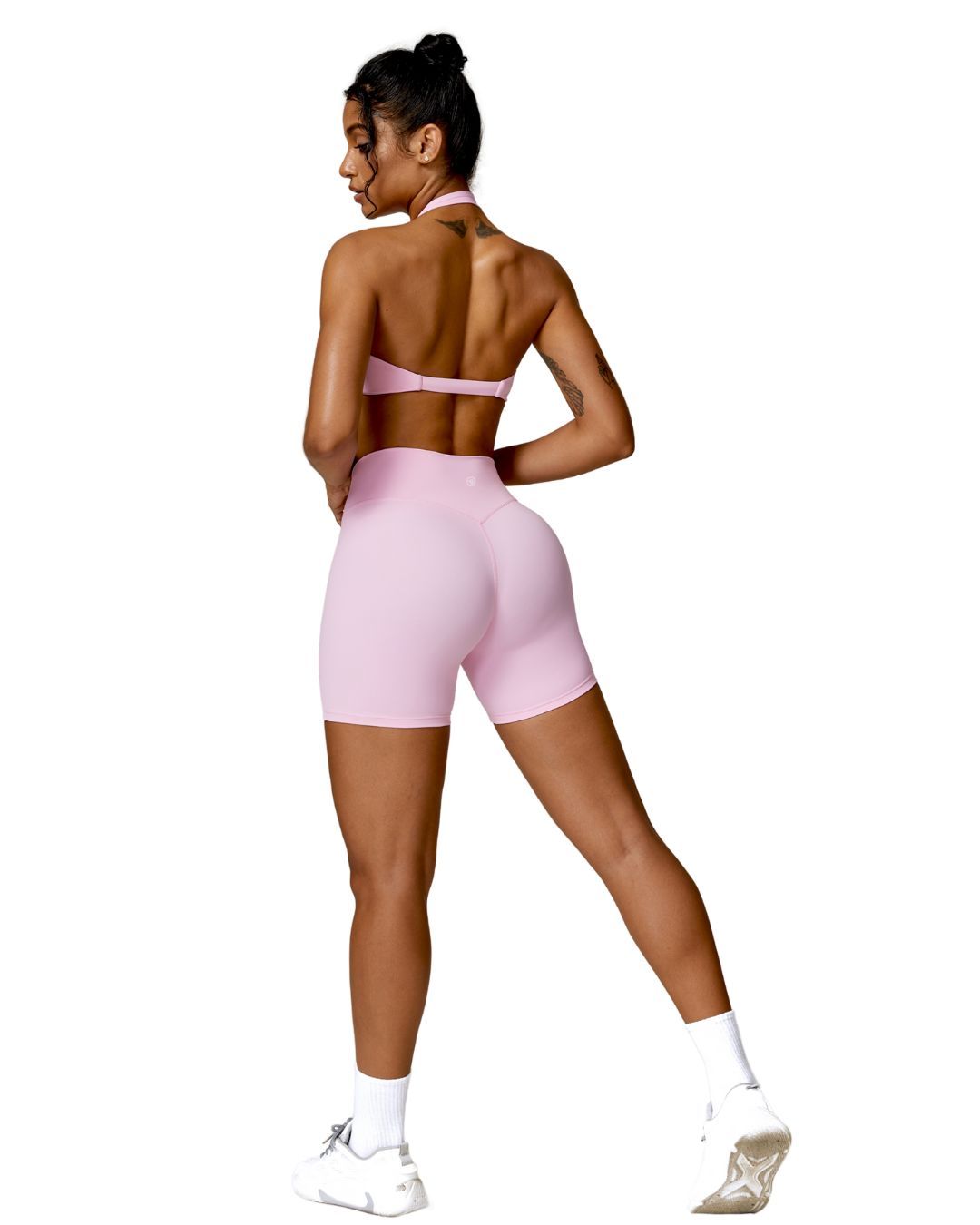 Woman wearing pink ORU MIKA SHORT with V-shaped back design, breathable fabric, and sculpting fit for gym or yoga.