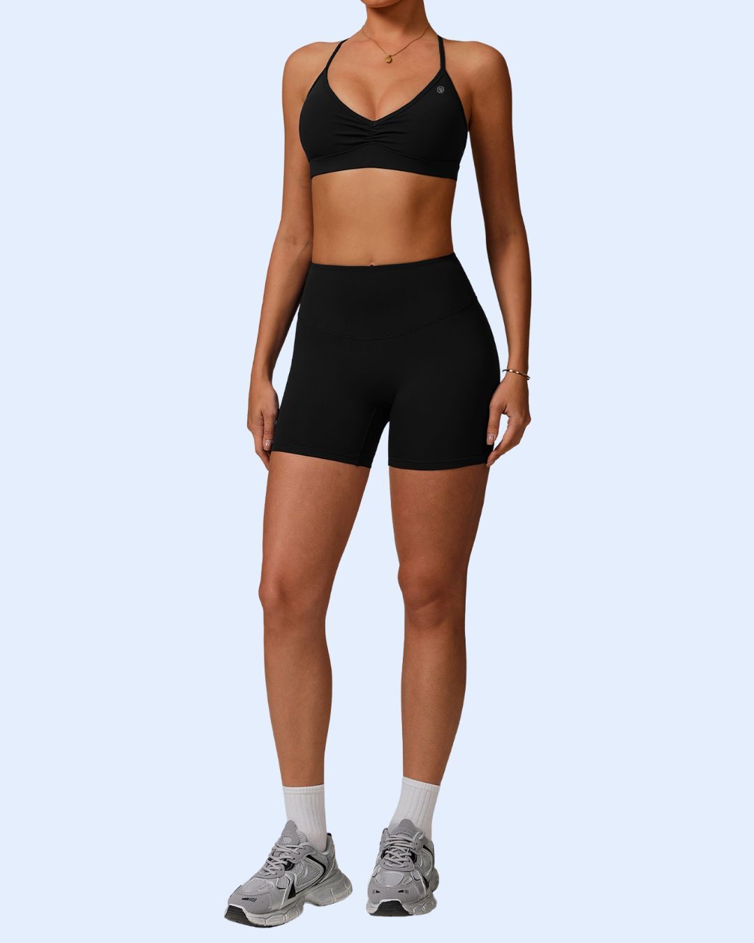 Woman wearing black ORU Phul Bra Top with narrow cross back straps and seamless fabric, paired with black shorts and gray sneakers