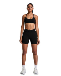 Woman wearing black ORU Elura short with high-rise waistband and sports bra standing against white background