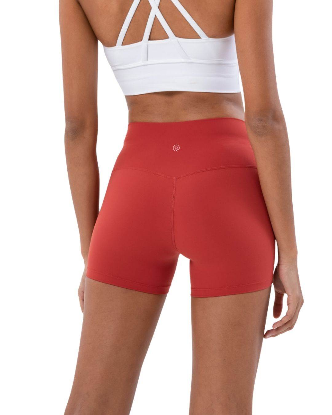 Woman wearing red ORU Mid-Rise Yoga Shorts showing subtle glute contour and slim fit design