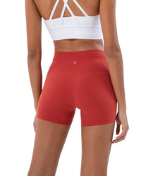 Woman wearing red ORU Mid-Rise Yoga Shorts showing subtle glute contour and slim fit design