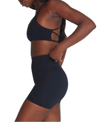 Woman wearing black ORU CROSSOVER SPORTS BRA with seamless design, strappy back, and matching high-waisted shorts.