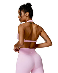 Woman wearing light pink ORU Mika Halter Sports Bra with halter neck support and matching high-waisted leggings, shown from the back.